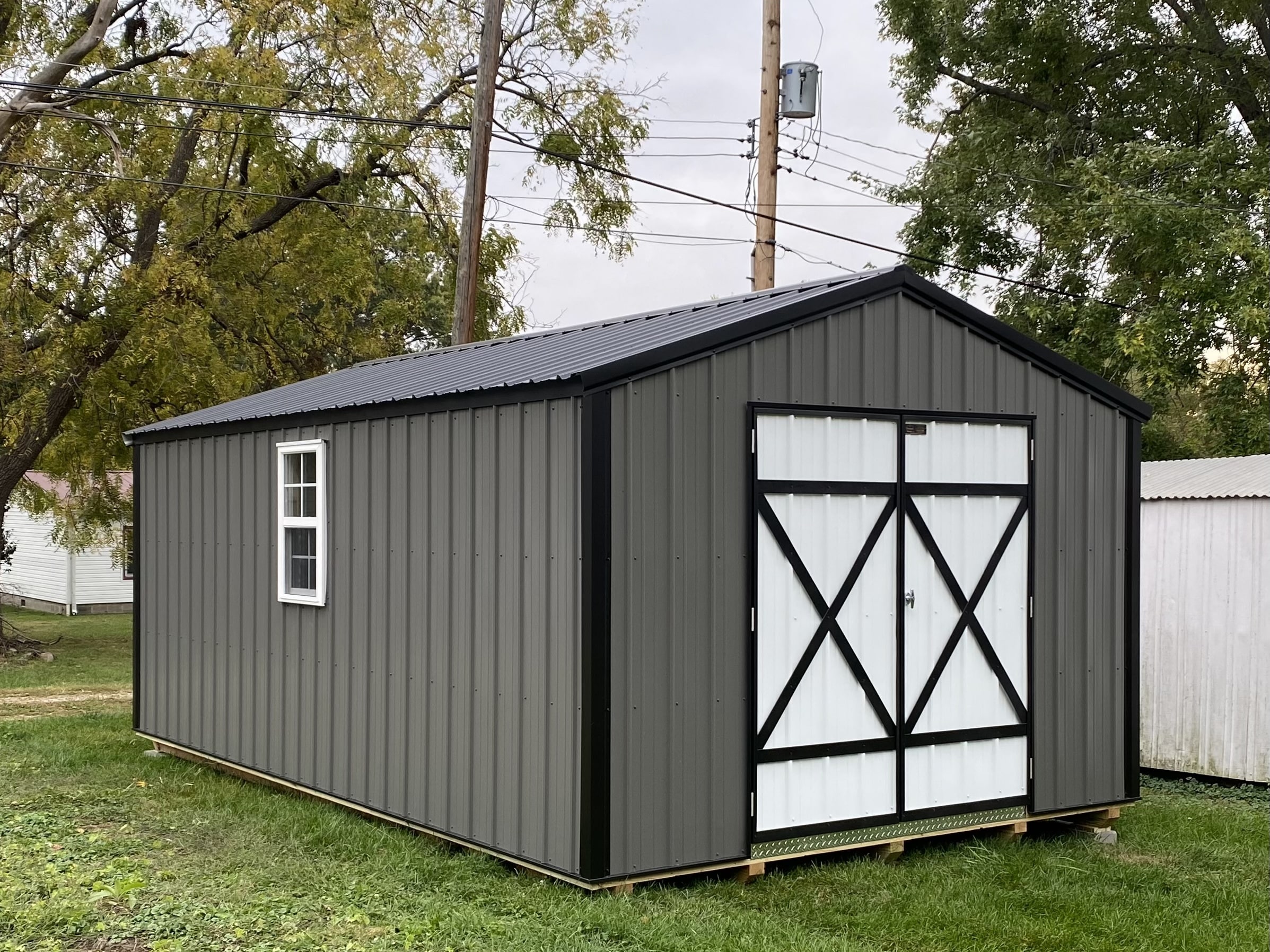 a grey metal storage shed with white double doors in Olathe KS