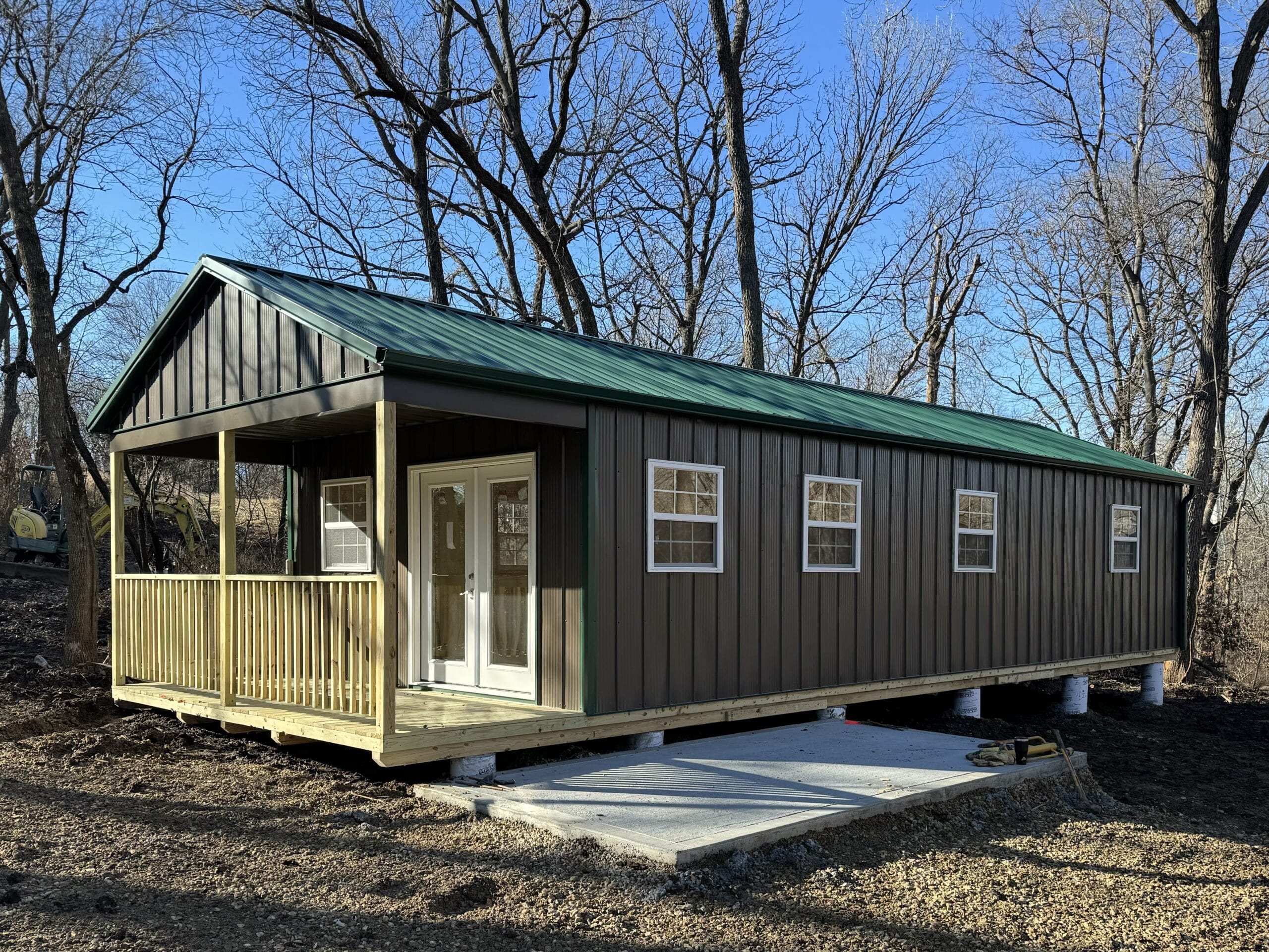 a brown cabin shed with a green roof and a front porch in the woods in Overland Park KS