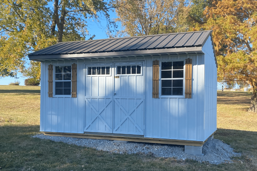 white garden shed with black metal roof and tan shutters